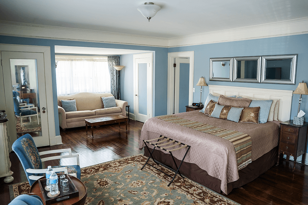 A cozy hotel room featuring a king-sized bed, a seating area, and large windows with natural light.