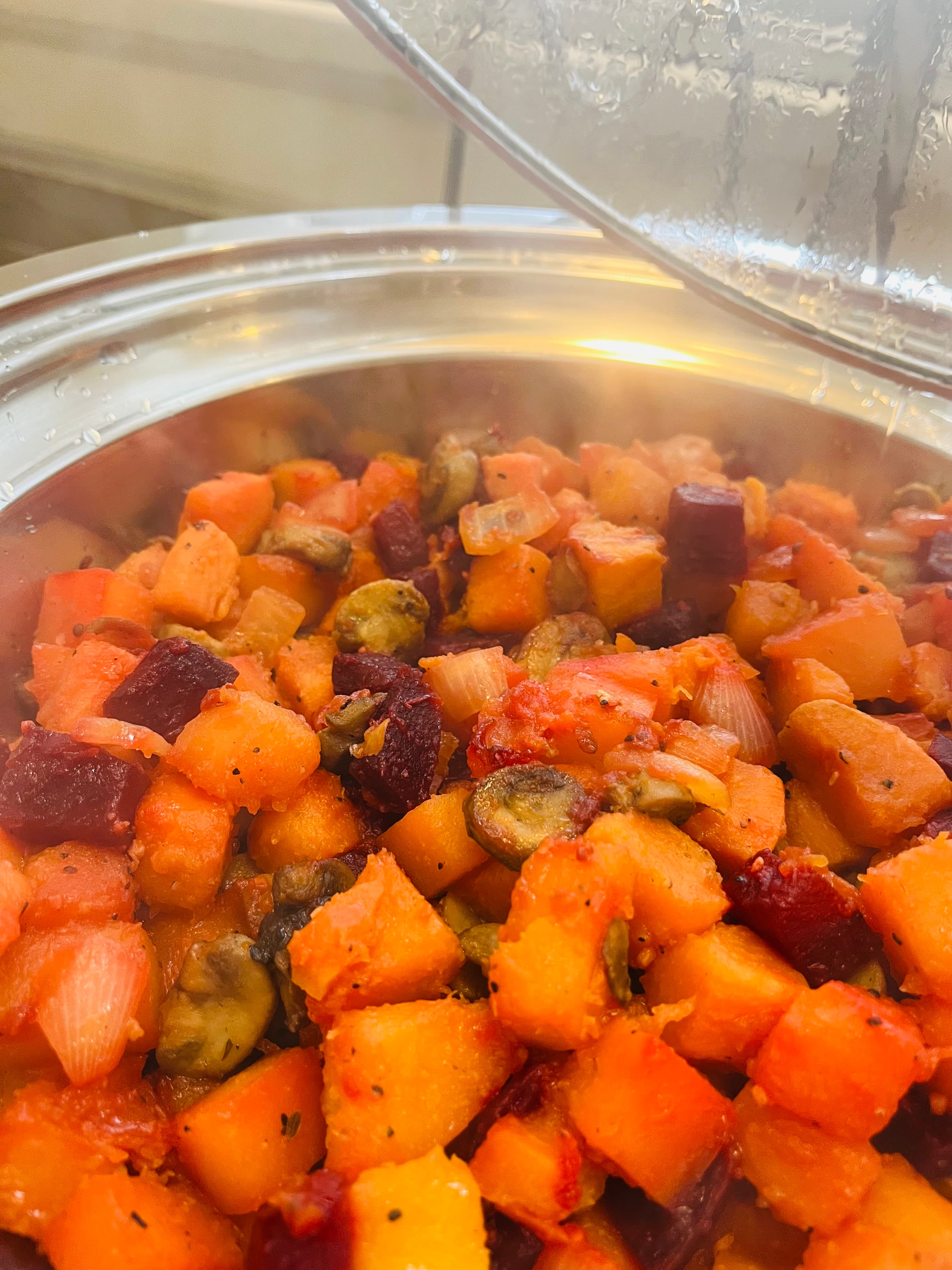 A close-up of a steaming pot filled with mixed diced vegetables, including orange squash and red beets.