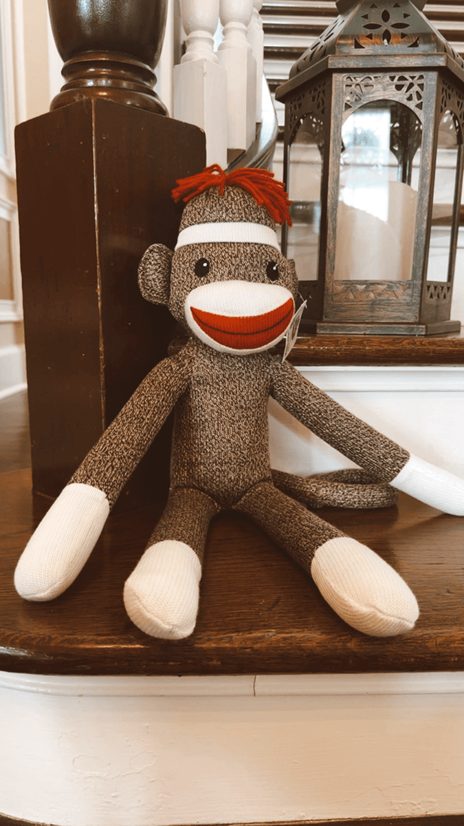 A plush sock monkey with a red mouth and hair sits on a wooden staircase beside a decorative lantern.