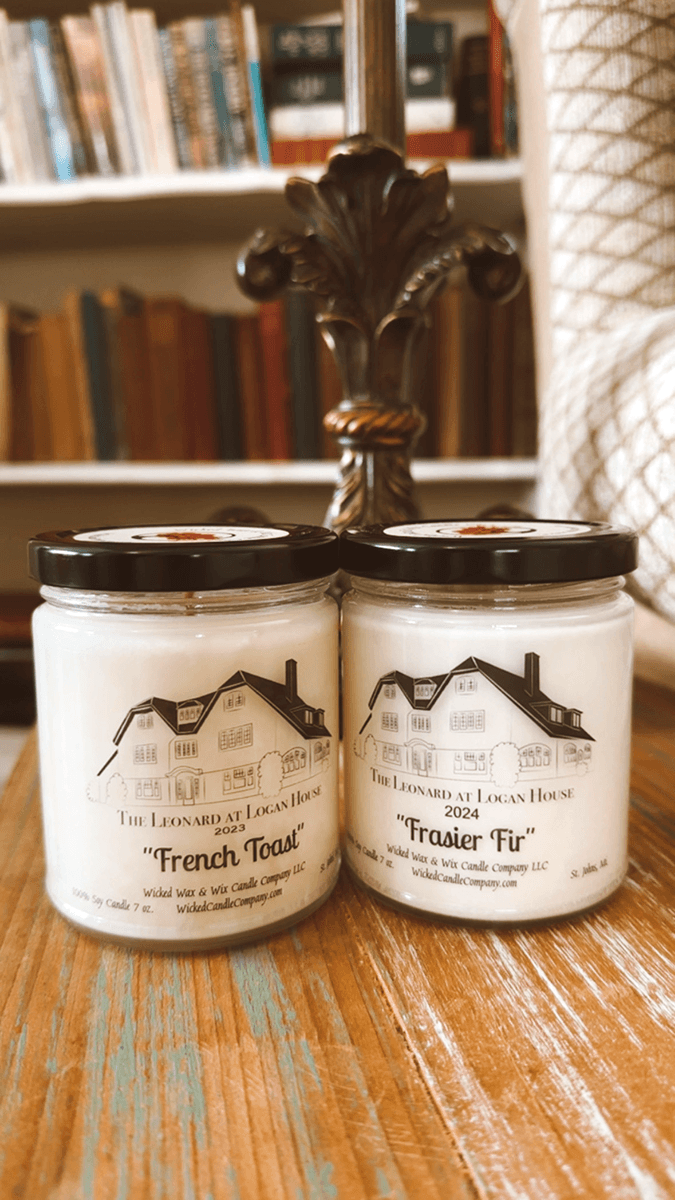 Two candle jars labeled "French Toast" and "Frasier Fir" on a wooden surface, with books in the background.