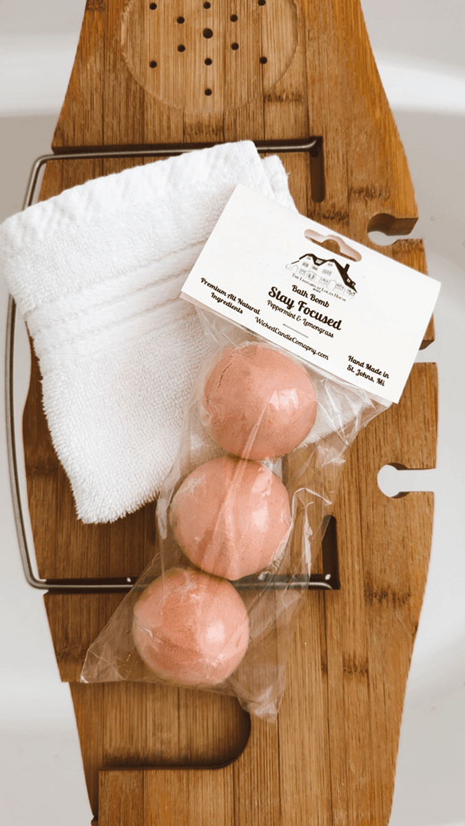 A wooden bath tray with three packaged bath bombs and a white towel.