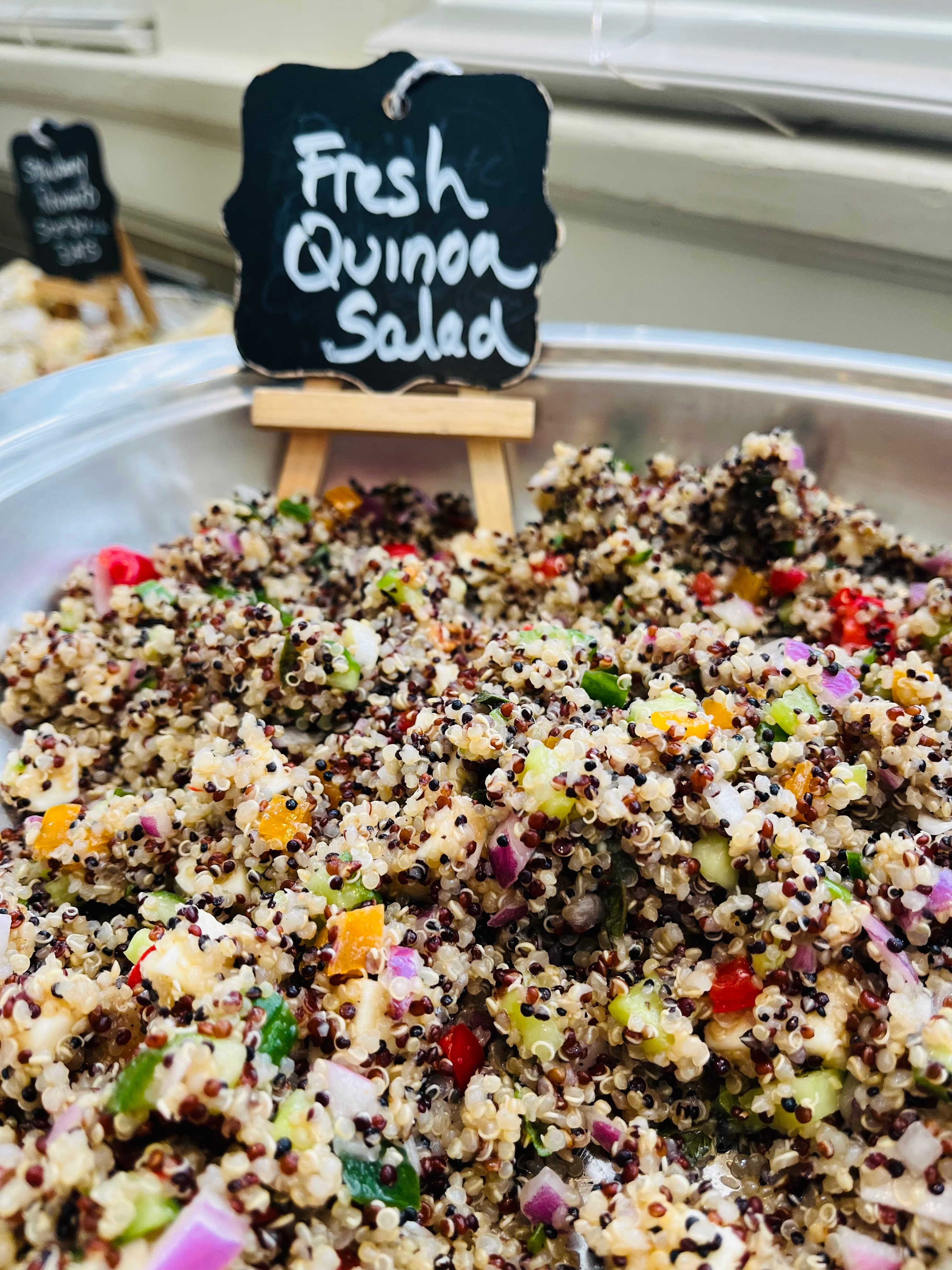 A close-up of a vibrant quinoa salad with various chopped vegetables and a sign labeling it as "Fresh Quinoa Salad."