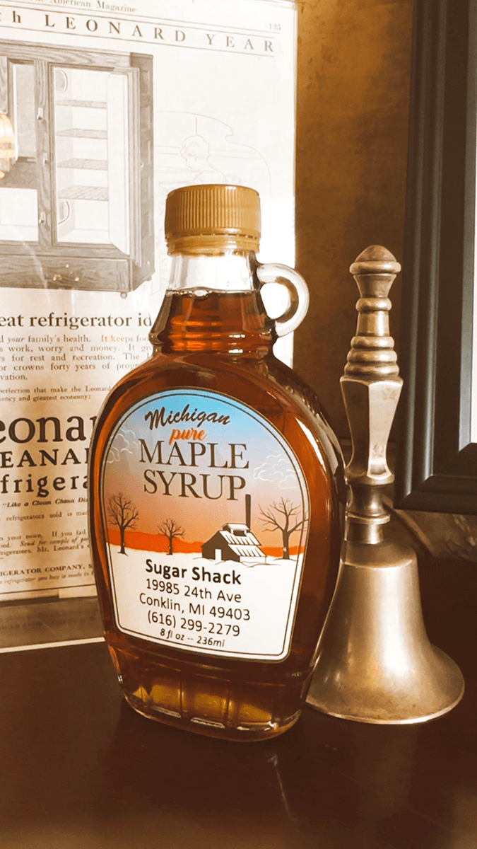 A bottle of Michigan pure maple syrup from Sugar Shack is displayed next to a bell and vintage magazine.