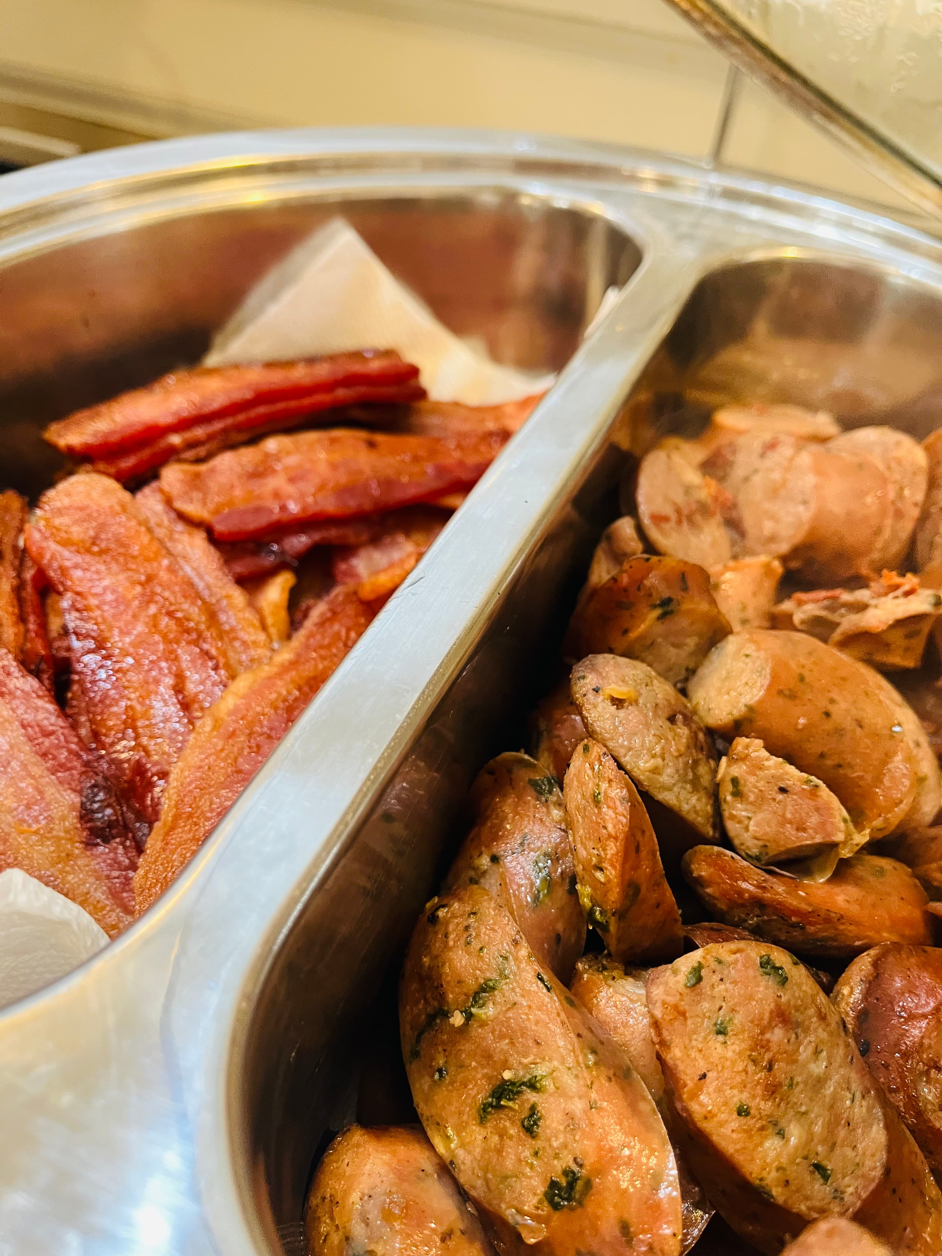 A stainless steel serving tray filled with two types of cooked sausages: crispy red and sliced brown.