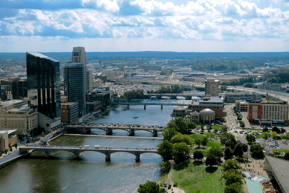 Aerial view of a city skyline featuring bridges over a river and lush green spaces.