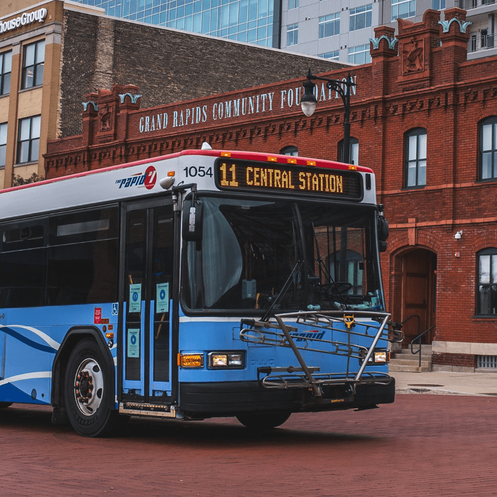 A blue public bus labeled "11 Central Station" stands in front of a brick building in Grand Rapids.