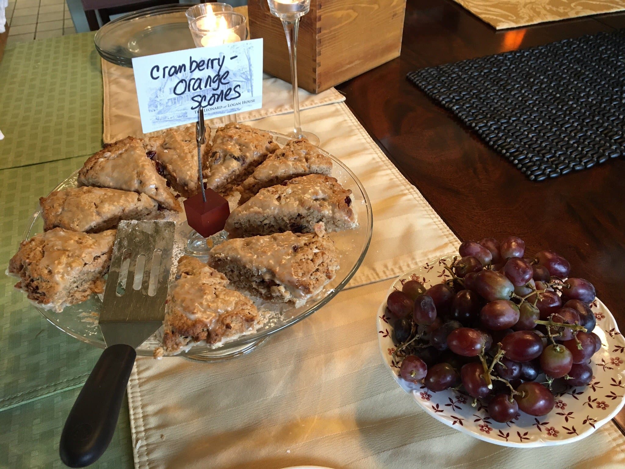 A plate of cranberry orange scones with a serving spatula, alongside a bowl of grapes.