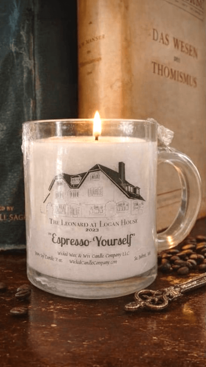 A lit candle in a glass mug labeled "Espresso-Yourself" sits near coffee beans and an antique key.