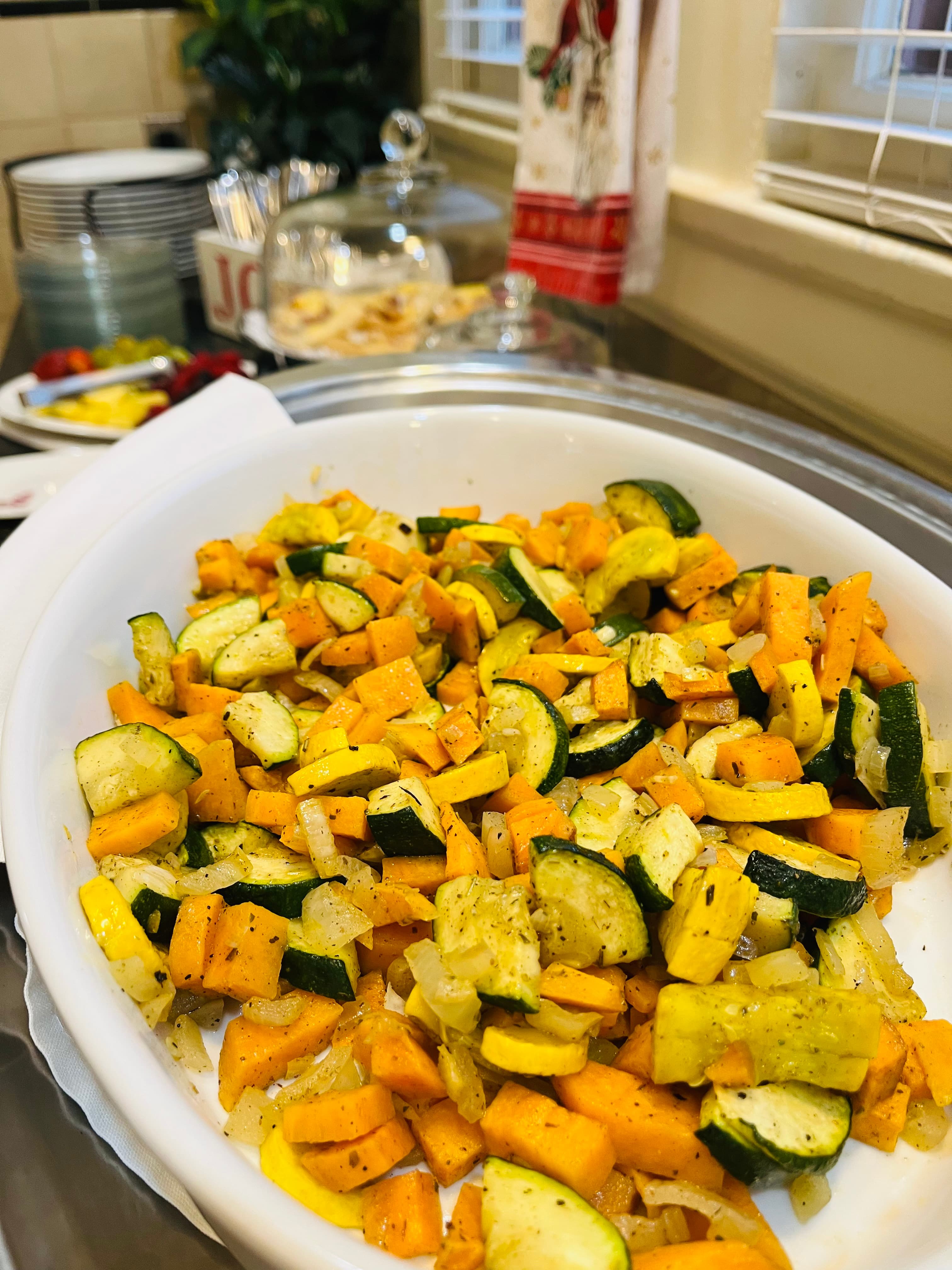 A dish of sautéed yellow squash, zucchini, and sweet potatoes garnished with onions.