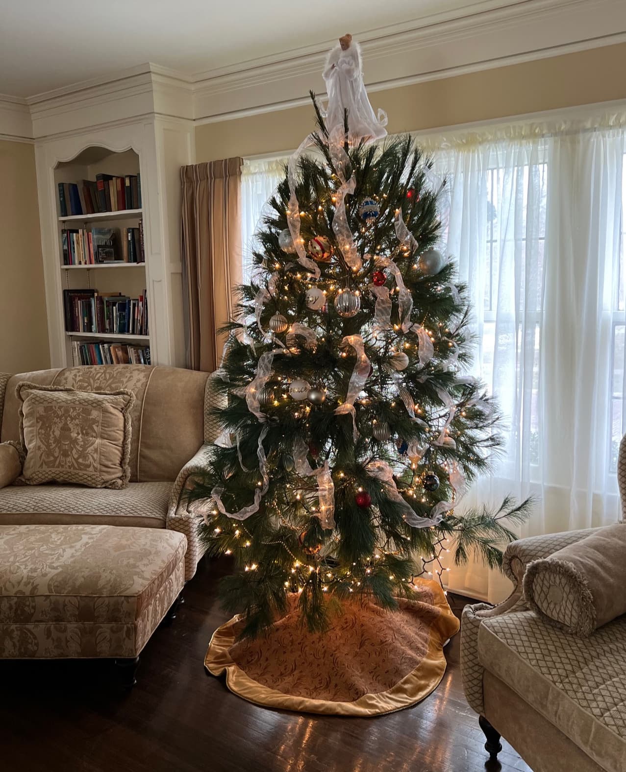 A decorated Christmas tree adorned with lights, white ribbons, and ornaments stands in a cozy living room. Soft light filters through the window, casting a warm, inviting glow. A decorated Christmas tree adorned with lights, white ribbons, and ornaments stands in a cozy living room. Soft light filters through the window, casting a warm, inviting glow.